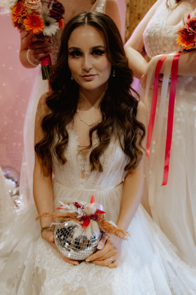 Braut im Hochzeitskleid mit Discokugel in der Hand.