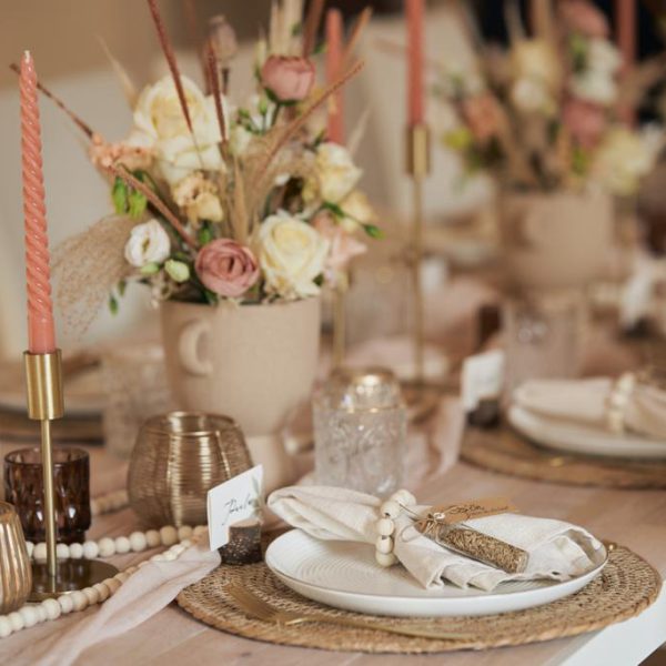 Blumengesteck auf einem Hochzeitstisch mit goldenen Kerzenständern und Teelichtern.