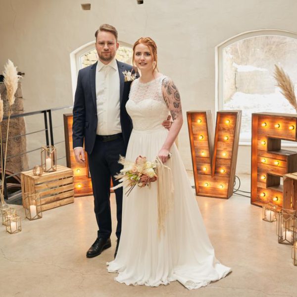 Brautpaar mit Love-Letter im Hintergrund bei ihrer Hochzeit.