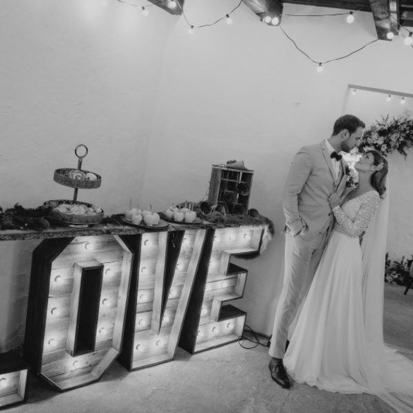 Brautpaar steht Arm in Arm vor leuchtenden Love Buchstaben in Schwarz Weiß